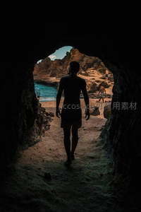 洞穴出口处剪影男子走向碧海沙滩的神秘瞬间