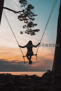 暮色海边树藤秋千上，女子剪影轻荡于绚烂晚霞之间