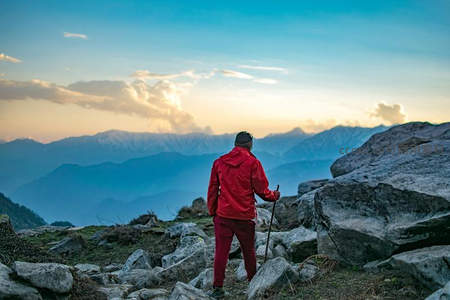 红衣登山者伫立山巅远眺层峦叠嶂，夕阳余晖映照壮丽 Himalayan 风景