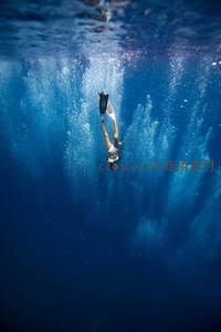 自由潜水者垂直下潜，气泡柱如光之瀑布贯穿深蓝水域