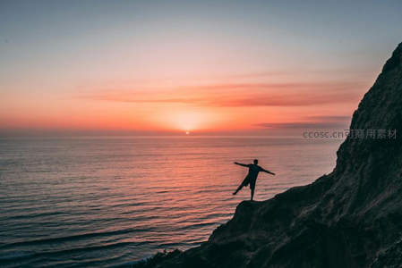 悬崖剪影迎日落海面，双臂展开定格自由与希望的瞬间