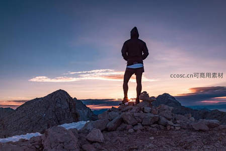 山顶石堆上孤影迎朝霞，紫蓝渐变天幕映衬征服者的剪影