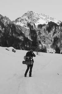 黑白影像中雪行者负重前行，巍峨雪山与密林构成肃穆背景