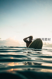 冲浪者浮于海面整理头发，夕阳余晖洒满波光