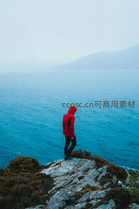 红衣旅人伫立海边悬崖，远眺雾霭中的苍茫海面与山影