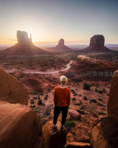 红岩峡谷观景台，金发旅人背对镜头眺望纪念碑谷三座巨柱，暮色温柔