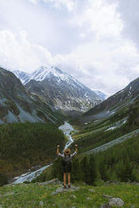 旅人立于山谷之巅张开双臂，俯瞰冰川融水蜿蜒穿行林海