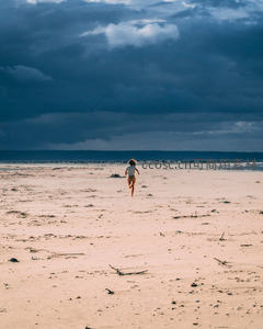 风暴将至：女孩赤足奔跑于空旷海滩，乌云压境