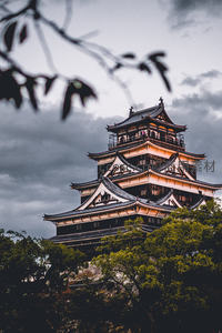 乌云密布下松本城雄姿透过前景枝叶若隐若现