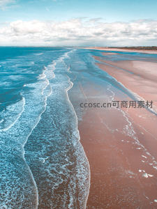 航拍视角下碧蓝海浪轻抚粉红沙滩，蜿蜒水痕勾勒海岸韵律