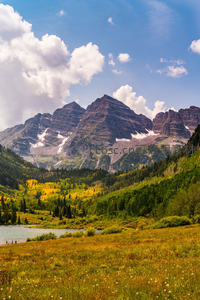 秋日阿斯彭山峰雪顶映衬金黄林海，湖畔草甸野花点缀如画