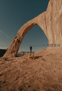 孤独旅人伫立天然砂岩拱门下，仰望苍穹与壮丽地貌