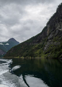 挪威峡湾航拍视角，陡峭岩壁绿植覆盖，船尾浪花划破幽深水面