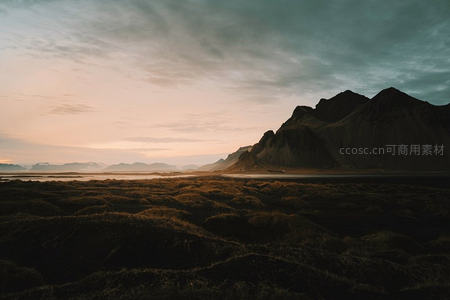 冰岛黑沙滩前苔原草丘日落，远山剪影与渐变天幕交织