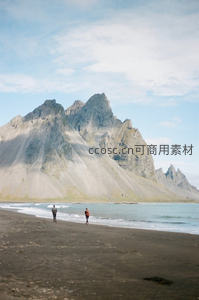 冰岛黑沙滩与尖峰山峦航拍风光，两人漫步海岸线