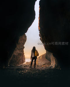 海蚀洞中剪影旅人远眺夕阳，光影交错海岸奇观