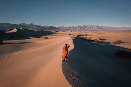 沙漠日落人像：橙裙女子伫立沙脊，远山剪影勾勒壮阔天地