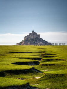 圣米歇尔山矗立潮间带，翠绿滩涂如波浪般延展至天际