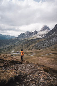 橙衣徒步者伫立山脊，俯瞰蜿蜒盘山路与连绵雪峰