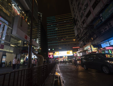 香港旺角夜市街景，霓虹灯牌林立，行人穿梭于潮湿街道