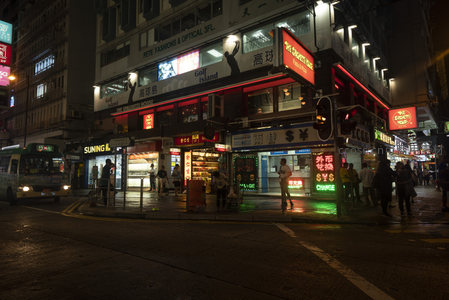 香港夜市街角霓虹闪烁，行人穿梭于商铺与公交之间