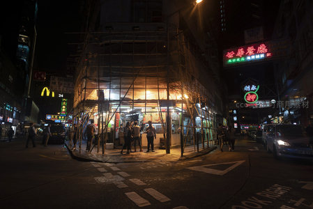 脚手架围裹的街角小吃摊，暖黄灯光下食客围坐夜宵时光