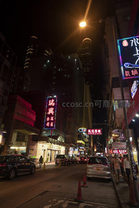 高楼夹缝中的霓虹街景，现代摩天楼与传统商铺共存的夜香港