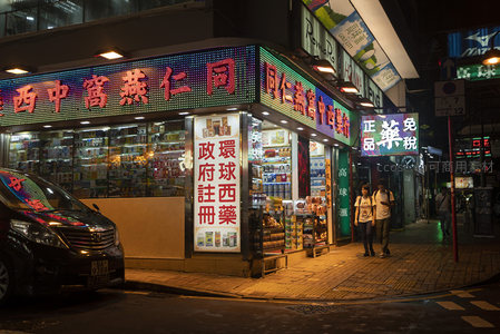 转角药房霓虹璀璨，行人漫步于香港夜间商业街角