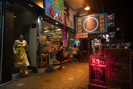 女士穿黄裙步出药房，霓虹招牌照亮港式街景