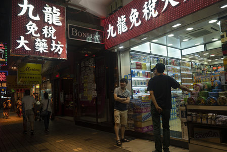 九龙免税大药坊夜市街景，霓虹招牌下行人驻足交谈