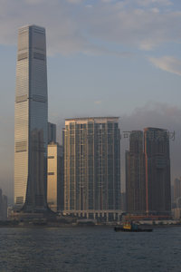 维港对岸摩天大楼林立，夕阳余晖镀金楼体，小船穿行水面如画