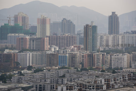 多层建筑群错落分布，施工塔吊矗立，远山环抱城市肌理