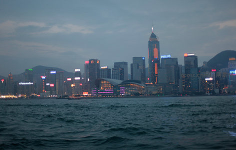 黄昏时分维港对岸灯火初上，中环天际线璀璨夺目倒映水面