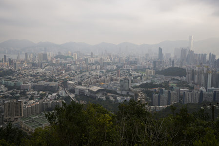 阴天下的香港城市全景，层叠楼宇与远山轮廓若隐若现