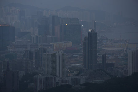 薄雾笼罩下的香港城市天际线，高楼林立，远山隐现
