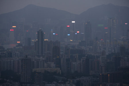 山峦环抱下的香港夜幕初临，霓虹广告牌穿透薄雾闪烁