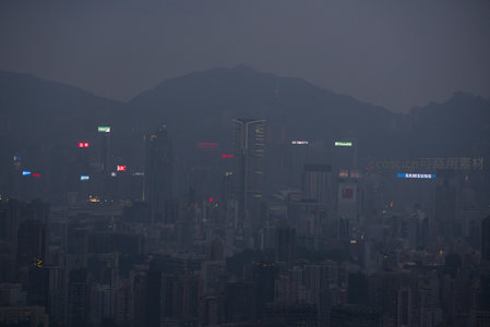 暮色中的香港维港天际线，高楼林立，霓虹初上，远山隐现于薄雾之中