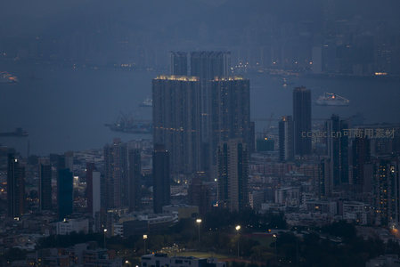 临海高层住宅群夜景特写，灯火映照海面，渡轮穿梭于港湾之间