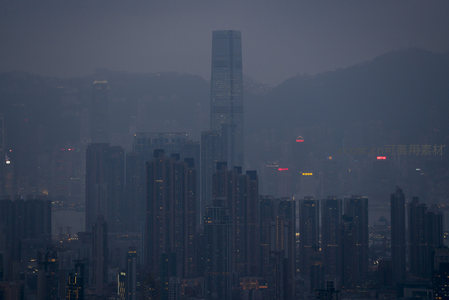 暮色中的香港天际线，高楼林立灯火初上，远山隐于薄雾之中