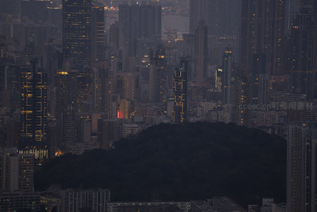 翠绿山丘嵌于钢筋森林中央，现代建筑群环绕，夜幕低垂光影交错