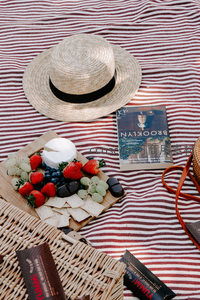 红白条纹野餐垫上的法式草帽与奶酪水果拼盘