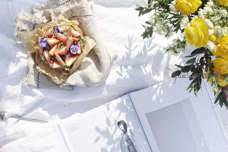 白色亚麻布上的春日甜点：草莓挞配黄玫瑰与时尚杂志