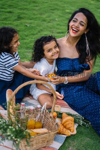 母亲与两女儿草地野餐欢笑时光，橙子传递温馨亲情瞬间