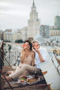 城市天台浪漫野餐：情侣手持西柚遮眼，背景莫斯科大学主楼