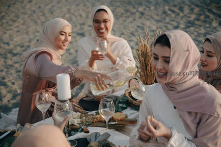 四位戴头巾女性沙滩野餐欢笑举杯共享温馨时光