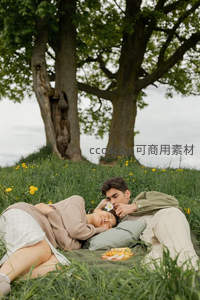 情侣躺卧草坡休憩，男子轻放小花于女子耳畔，静谧温柔