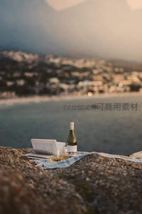 岩石高处野餐：白葡萄酒、书本与海岸小镇朦胧夜景