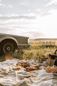 复古轿车旁田野野餐，格纹布上摆满奶酪面包与红酒，夕阳洒落金辉