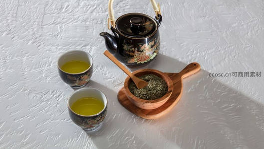 黑釉彩绘茶壶配青瓷茶杯与干茶叶，置于纹理白布之上静谧雅致