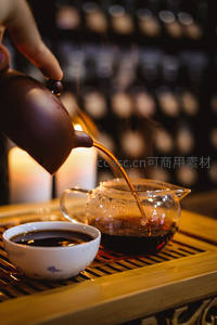 紫砂壶倾注茶汤入公道杯，烛光摇曳间茶席氤氲，展现传统工夫茶仪式